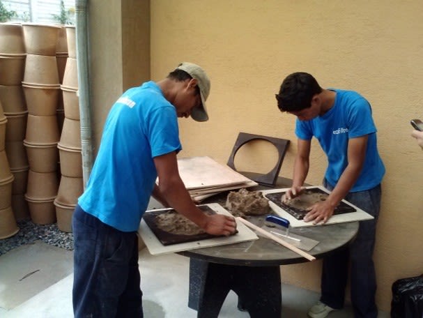 Image of a two men wearing blue tshirts, shaping cement filters in a mould.