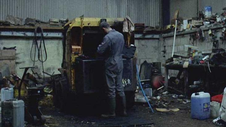 A still from the film 'Landline' showing a young farmer doing maintenance on his Land Rover