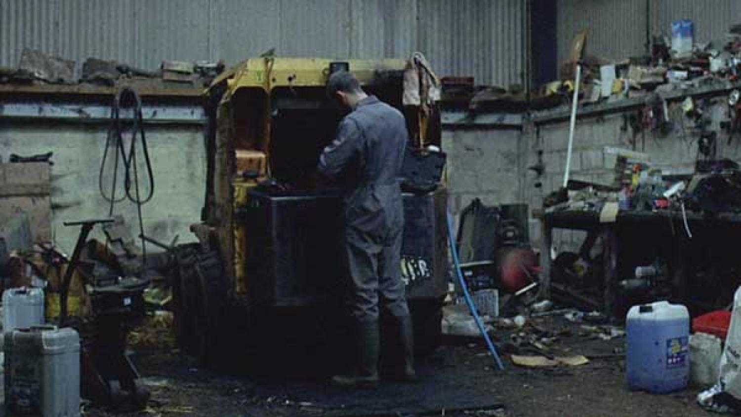 A still from the film 'Landline' showing a young farmer doing maintenance on his Land Rover