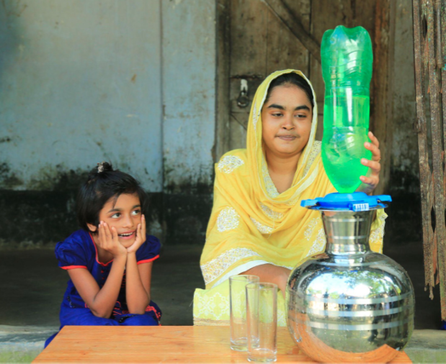 A youn g child watching anothether child demonstrating the use of a water filter 
